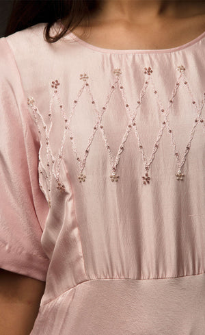 Graceful, demure and classic simplicity, this powder pink ensemble features a geometric hand embroidery on the mid yoke of this floor length flowing gown. Adorned with understated combination of peachy and translucent beads and threads, this cupro satin piece is yet a delicately detailed silhouette. 