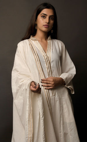 The muse is wearing a classic kurta set style, enhanced with added godet panels. This kurta is crafted in 100% cotton, is delicately embroidered with aari zari work paired with relaxed palazzos and accompanied by a 100% cotton dupatta embroidered with a coordinating zari border. 