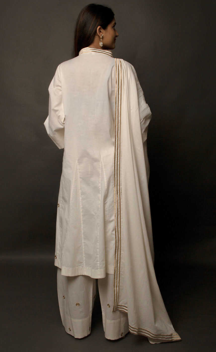 The muse is wearing a classic kurta set style, enhanced with added godet panels. This kurta is crafted in 100% cotton, is delicately embroidered with aari zari work paired with relaxed palazzos and accompanied by a 100% cotton dupatta embroidered with a coordinating zari border. 