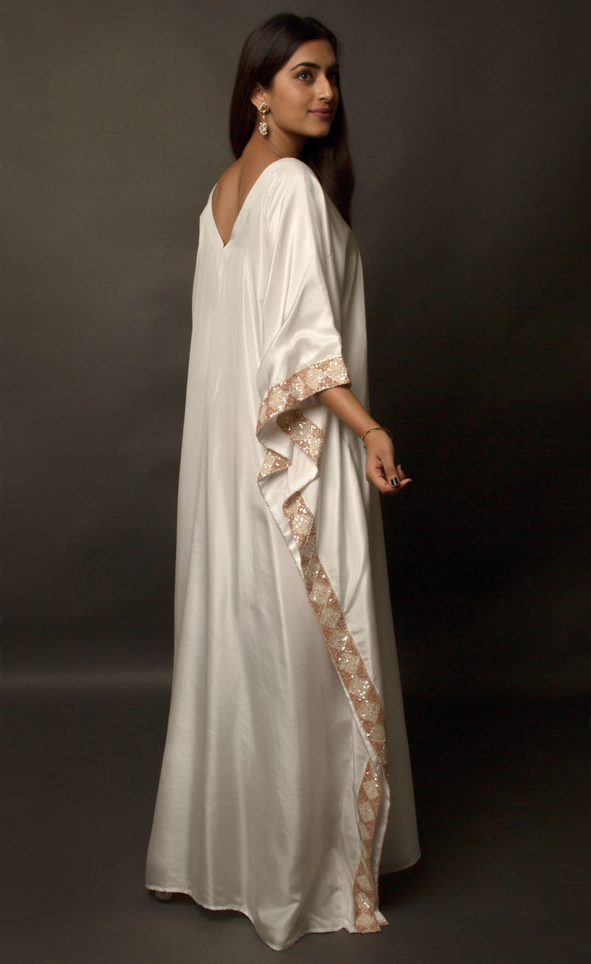 The muse is seen here wearing a classic V neck satin kaftan hand embellished with sequins and beads. The bordered embroidery beautifully runs along the length of the satin kaftan and also along its relaxed sleeves. The embellishments are all tonal shades of peach and off white. 